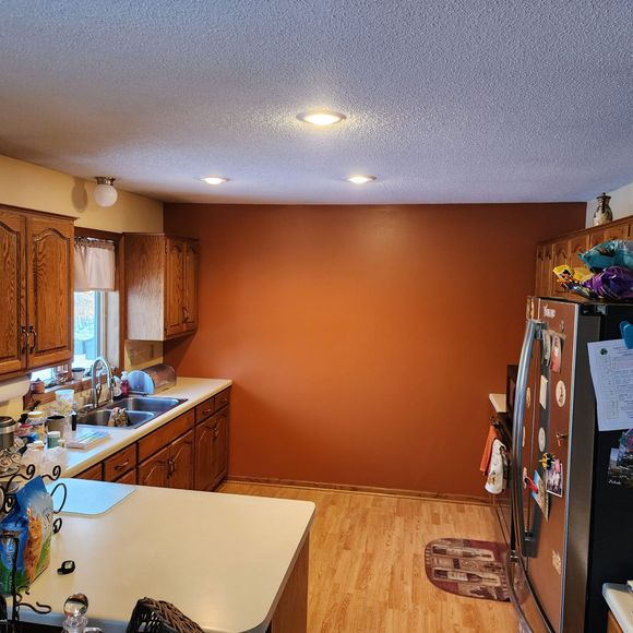 Kitchen with orange accent wall, wood cabinets, white countertop, and stainless steel refrigerator.