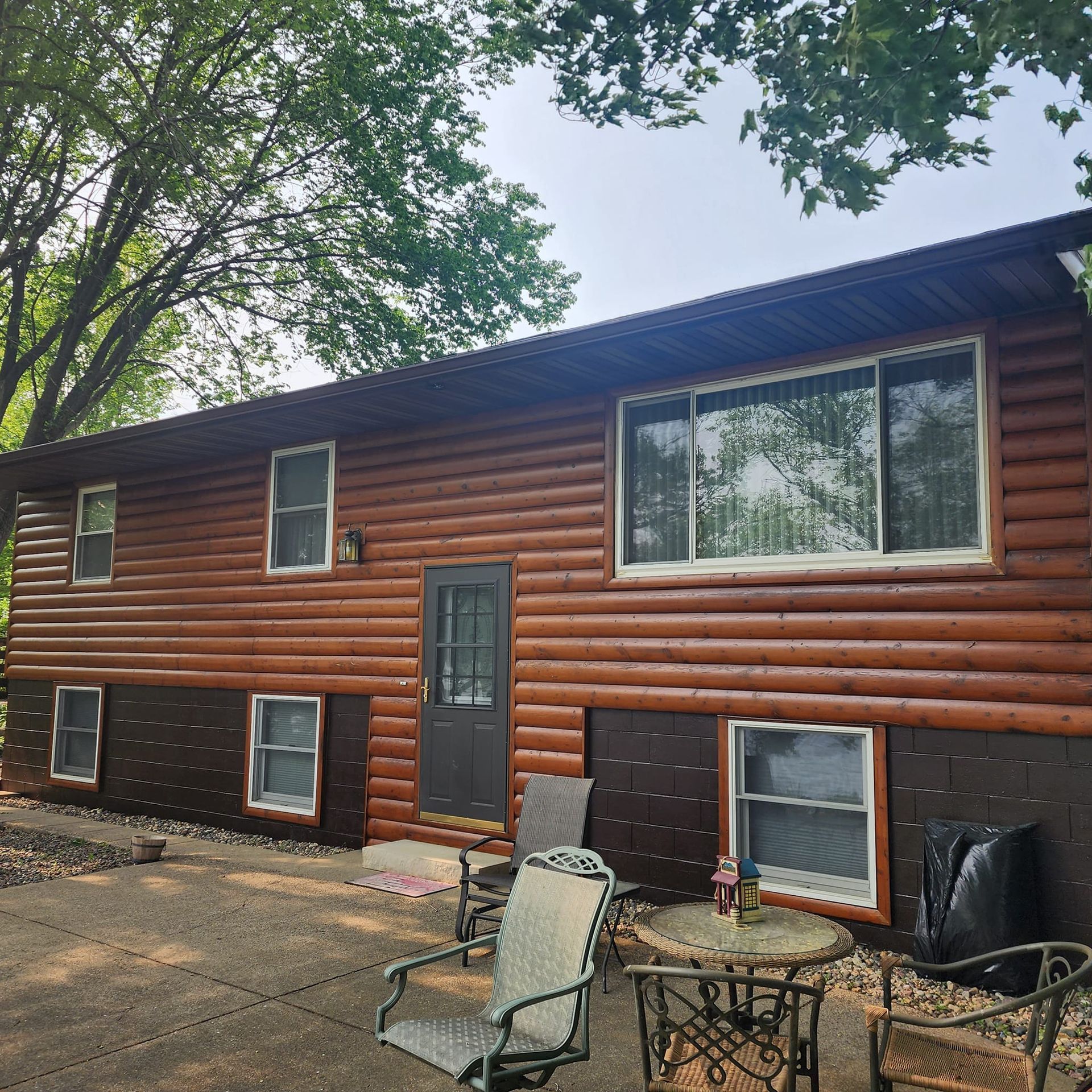 Two-story log cabin with brown siding, dark brown accents, and a patio with outdoor furniture.