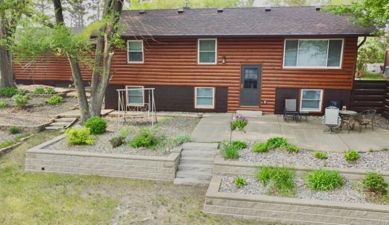 Brown house with stone retaining walls, front patio, landscaping, and steps.