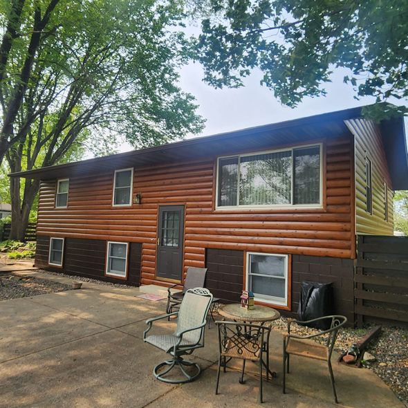 Brown log-sided house with a patio and outdoor furniture. Dark brown lower siding, light brown upper.