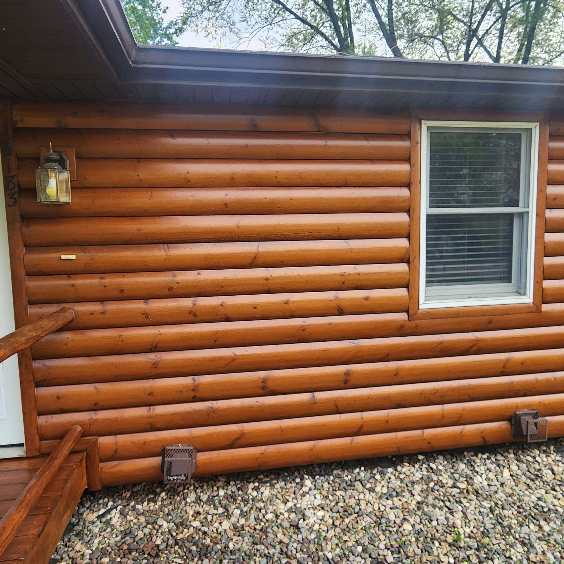 Brown log cabin exterior with window, light fixture, and pebble ground.