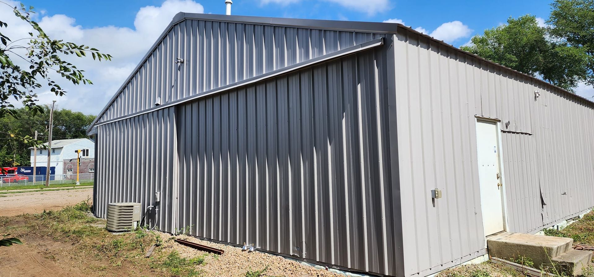 A gray metal building with a door in a rural setting on a sunny day.