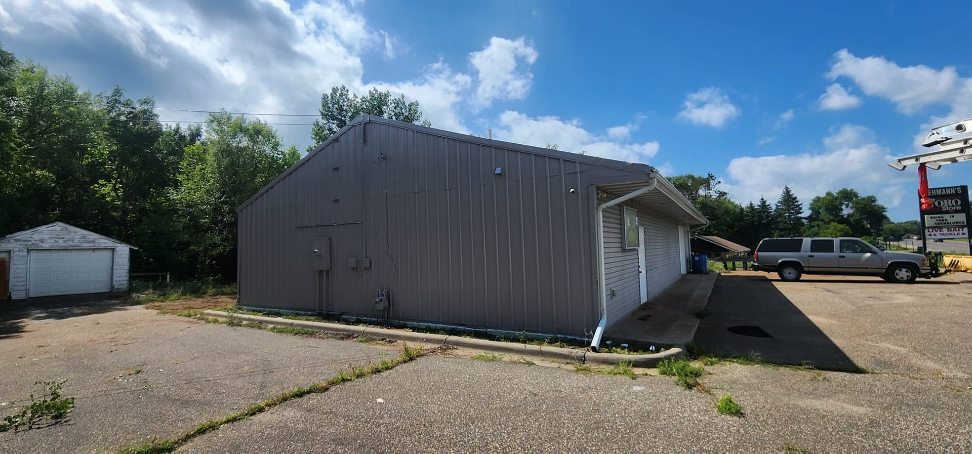 Gray industrial building and garage with a pickup truck parked out front. Blue sky with clouds.