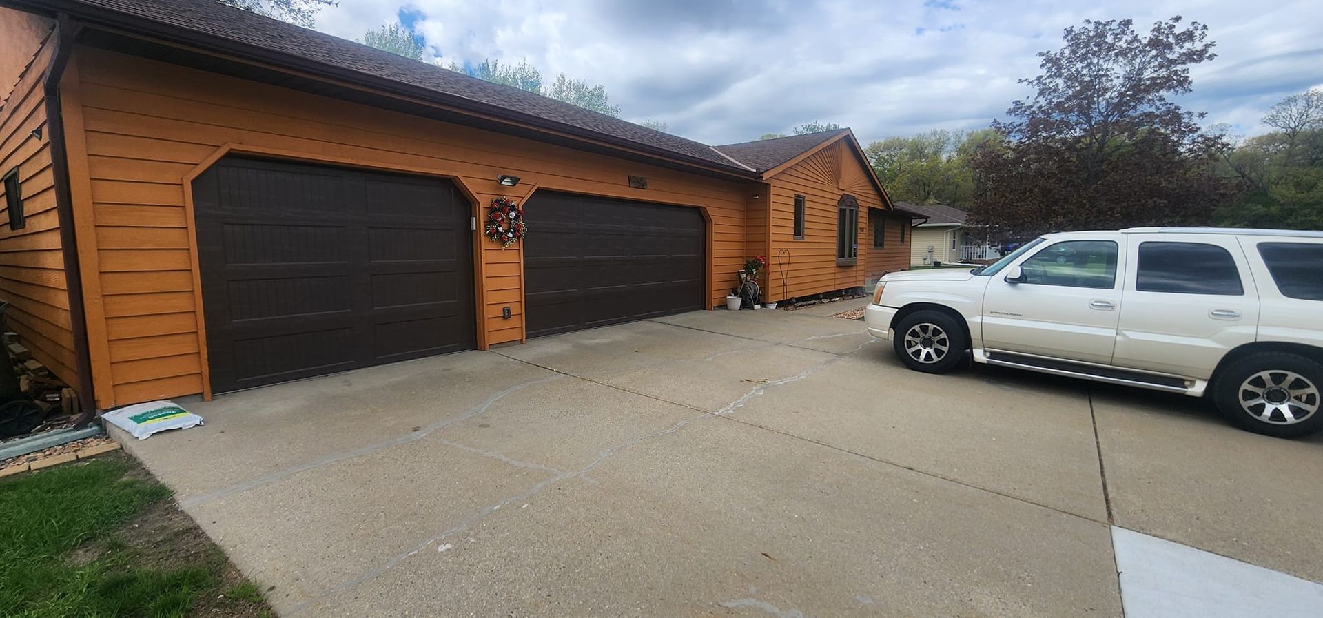 A tan house with brown garage doors and a white SUV parked in the driveway.