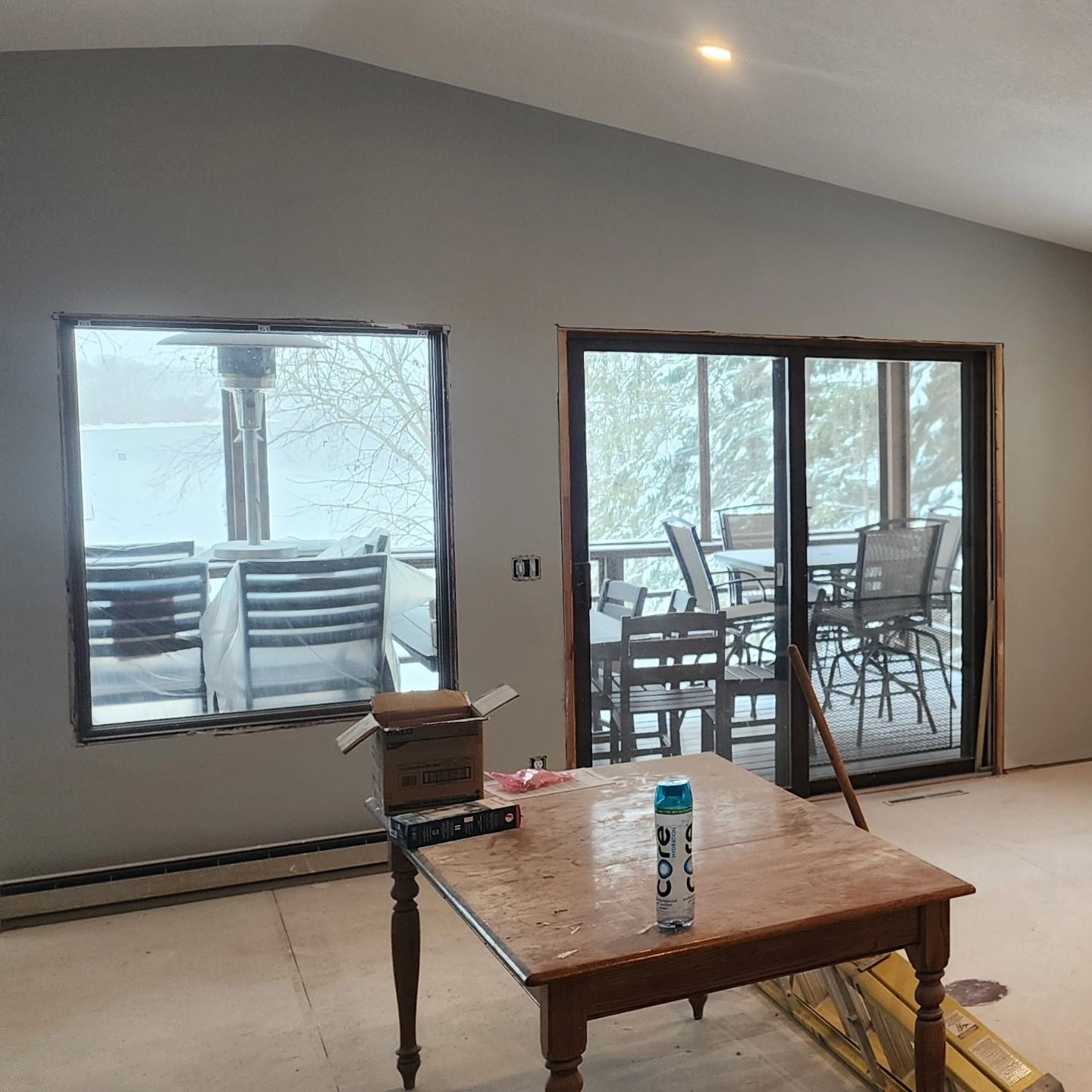 Interior of a room with large windows, overlooking snow-covered deck. A wooden table is in the foreground.