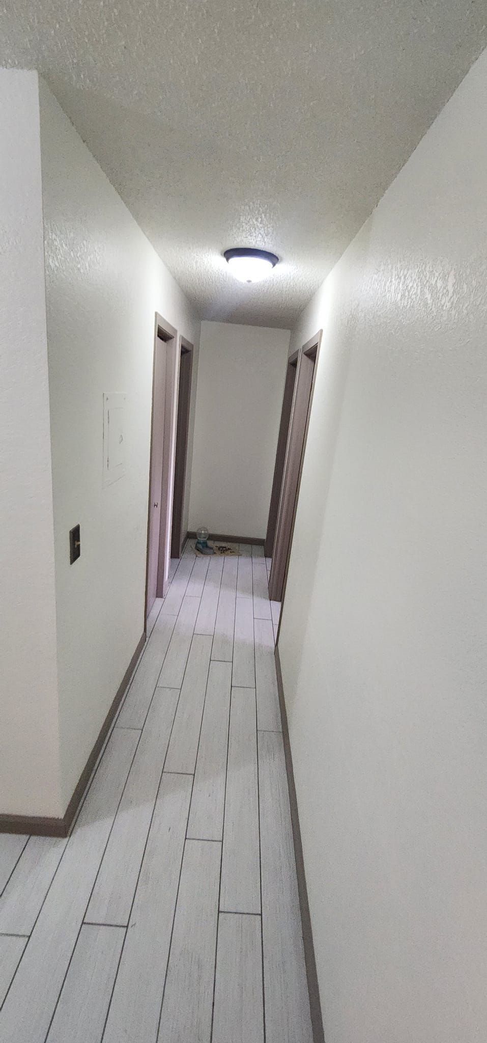 Narrow hallway with white walls, a patterned floor, and doors at the end.