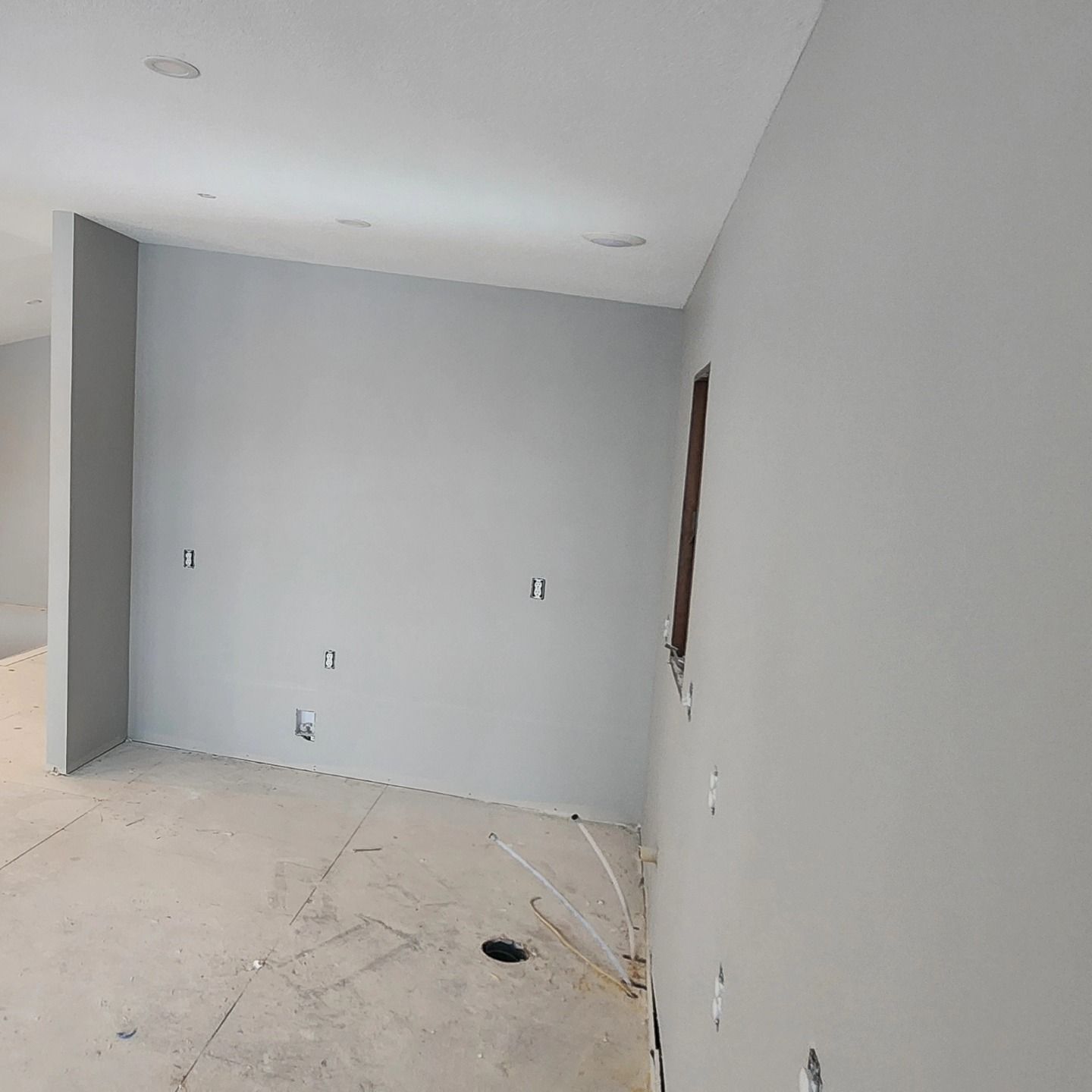 Empty room under construction, gray walls, unfinished floor, visible electrical outlets.