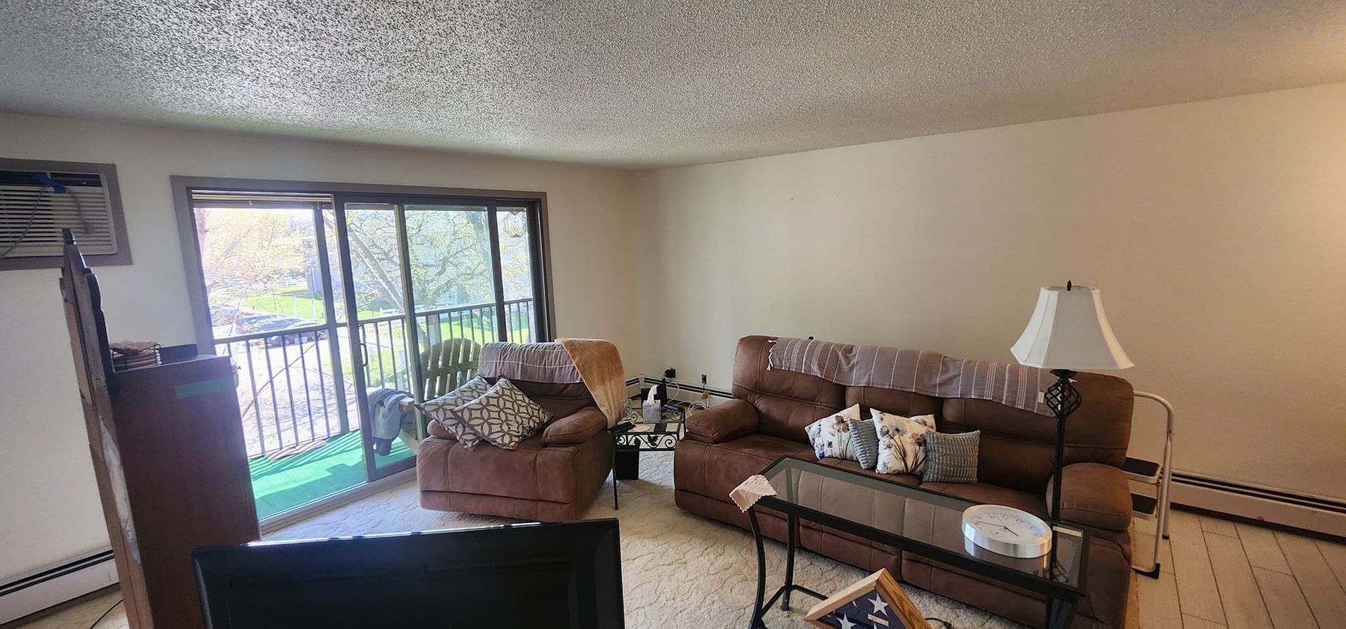 A brown living room with a couch, armchair, sliding glass door, and a lamp.
