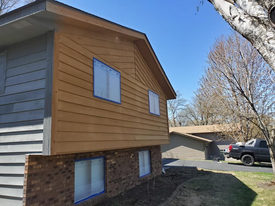House exterior with brown wood siding, gray siding, brick base, blue sky, and a truck.