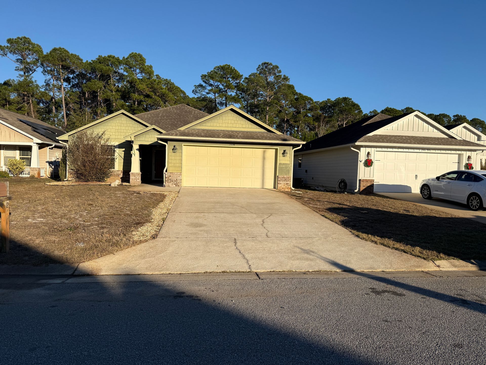 House with light green siding and a cracked driveway, surrounded by brown yard and other houses.