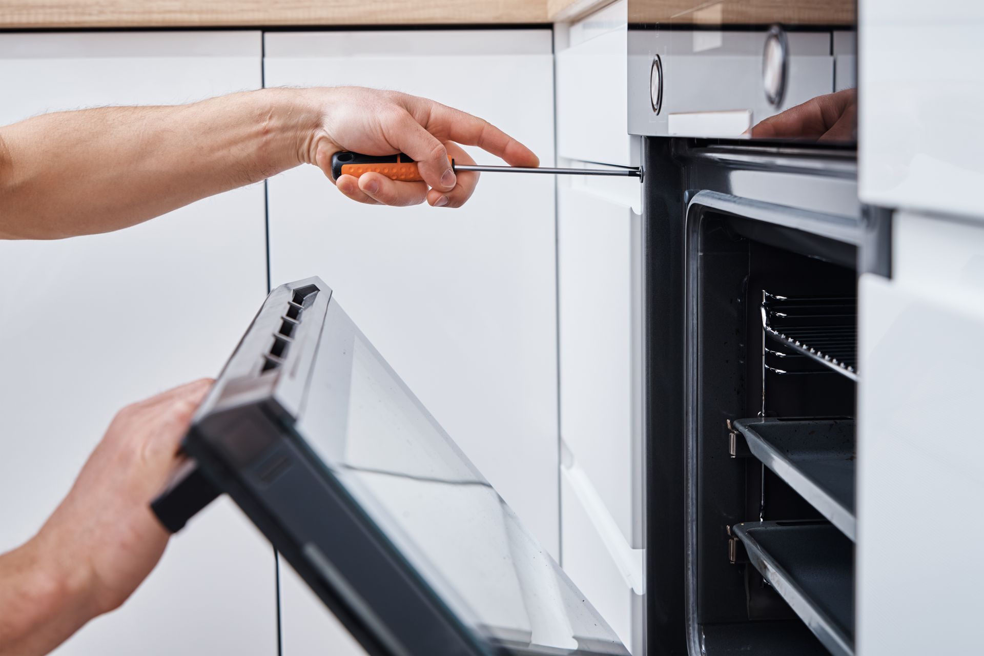 A person is fixing an oven with a screwdriver.