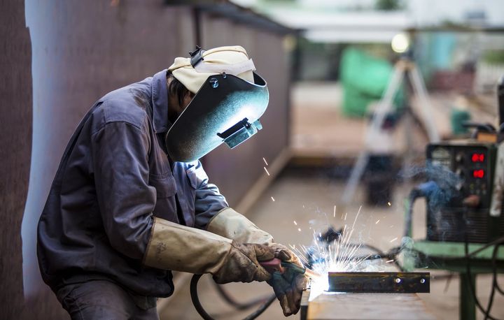 A man wearing a welding mask is welding a piece of metal.