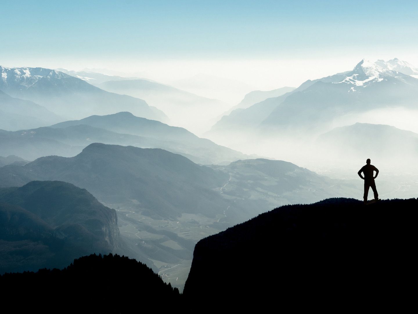 Silhouette of person standing on cliff overlooking mountains in the mist.