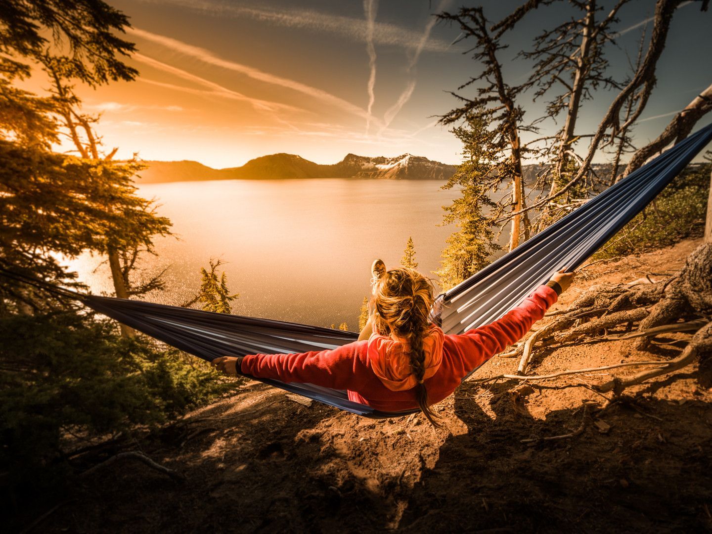 Person in a hammock, overlooking a lake and mountains at sunset.