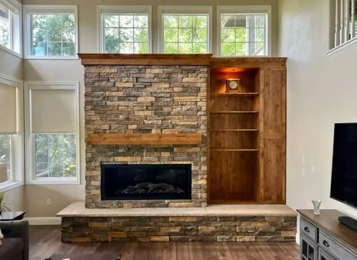 Stone fireplace with built-in wooden shelving; windows above, electric fireplace insert.