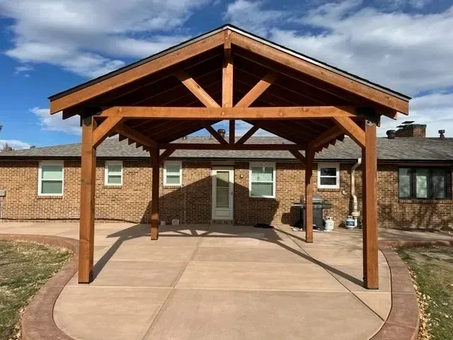 Wooden patio cover extending from a brick house, over a concrete patio.