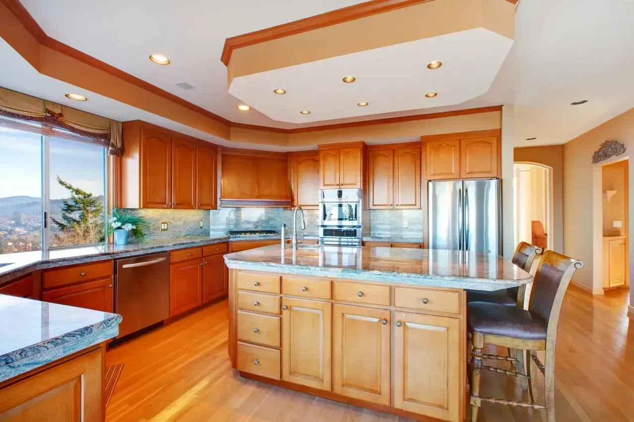 Kitchen with wooden cabinets, stainless steel appliances, and island with bar stools.