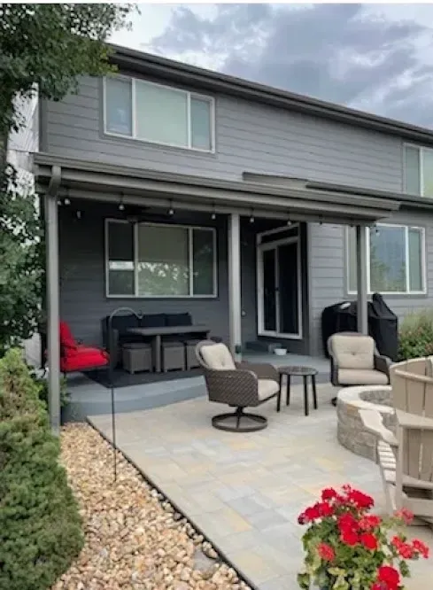 Backyard patio with seating, fire pit, and a covered porch attached to a gray house.