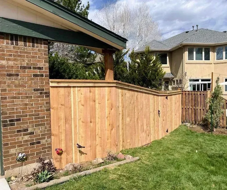 Wooden fence with a brick house section and green lawn.