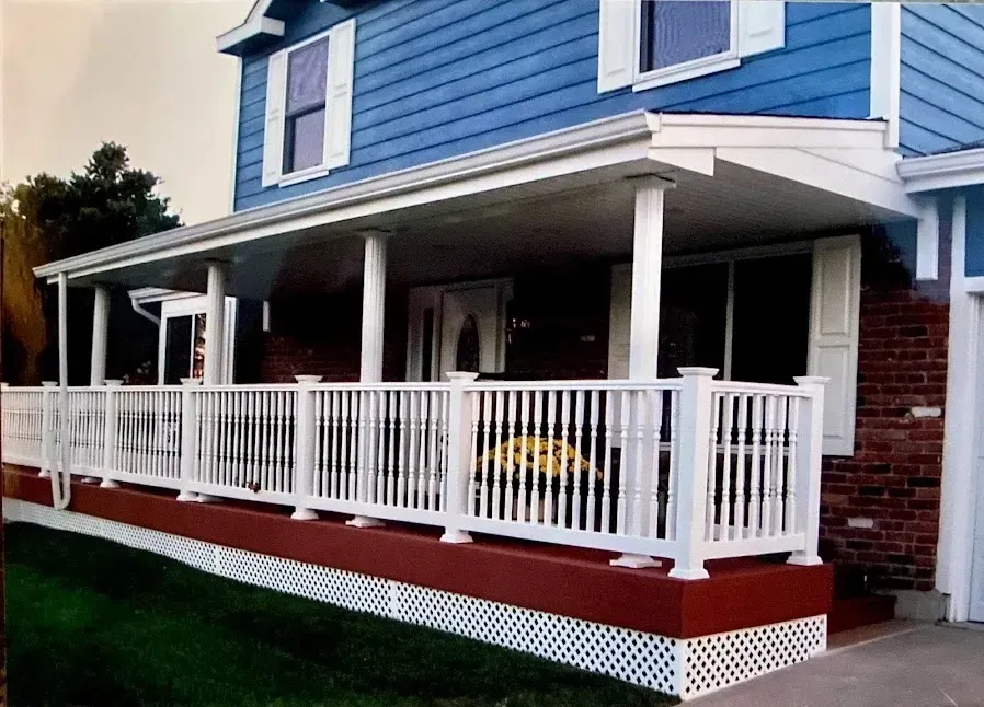 Blue house with white porch, railing, and columns; red base with lattice; green grass.