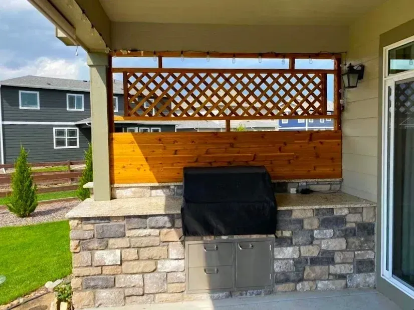 Outdoor kitchen with a grill, stone facade, and lattice wooden screen.