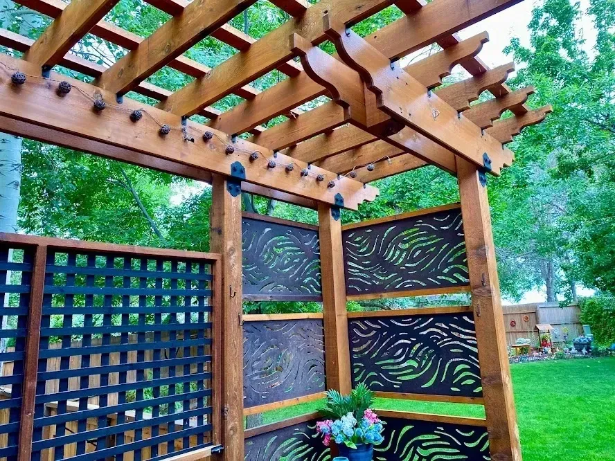 A wooden pergola with black lattice and decorative patterned screens in a garden setting.