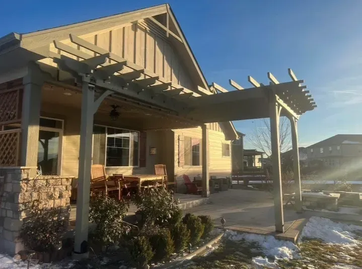 Beige house with pergola and outdoor seating on a sunny day with snow on the ground.