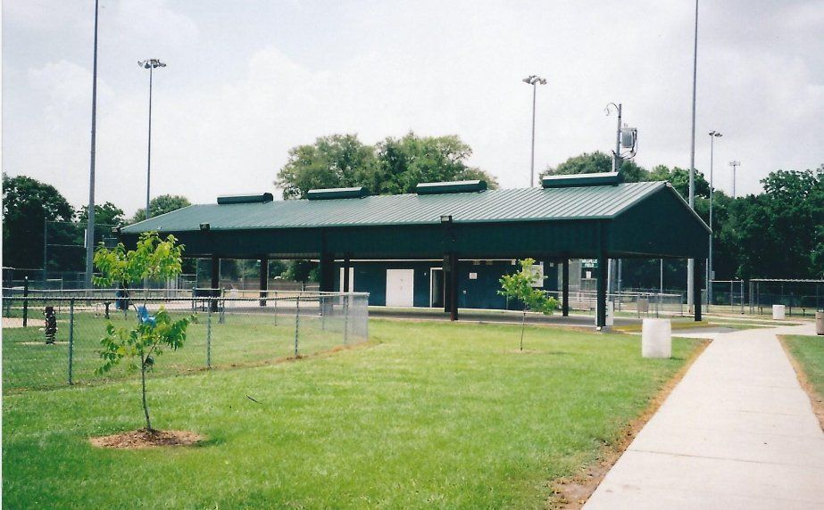 Green park pavilion with benches and a sidewalk beside a fenced sports field