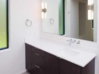 A modern bathroom vanity with a white countertop, dark cabinets, and a large mirror.