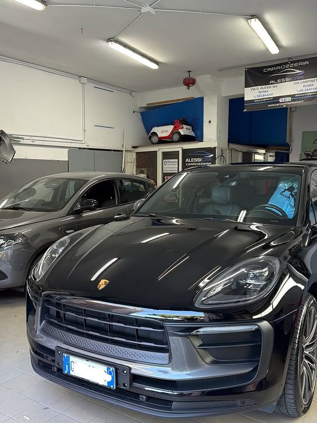 Un SUV Porsche nero e un'auto grigia all'interno di un'autofficina ben illuminata.