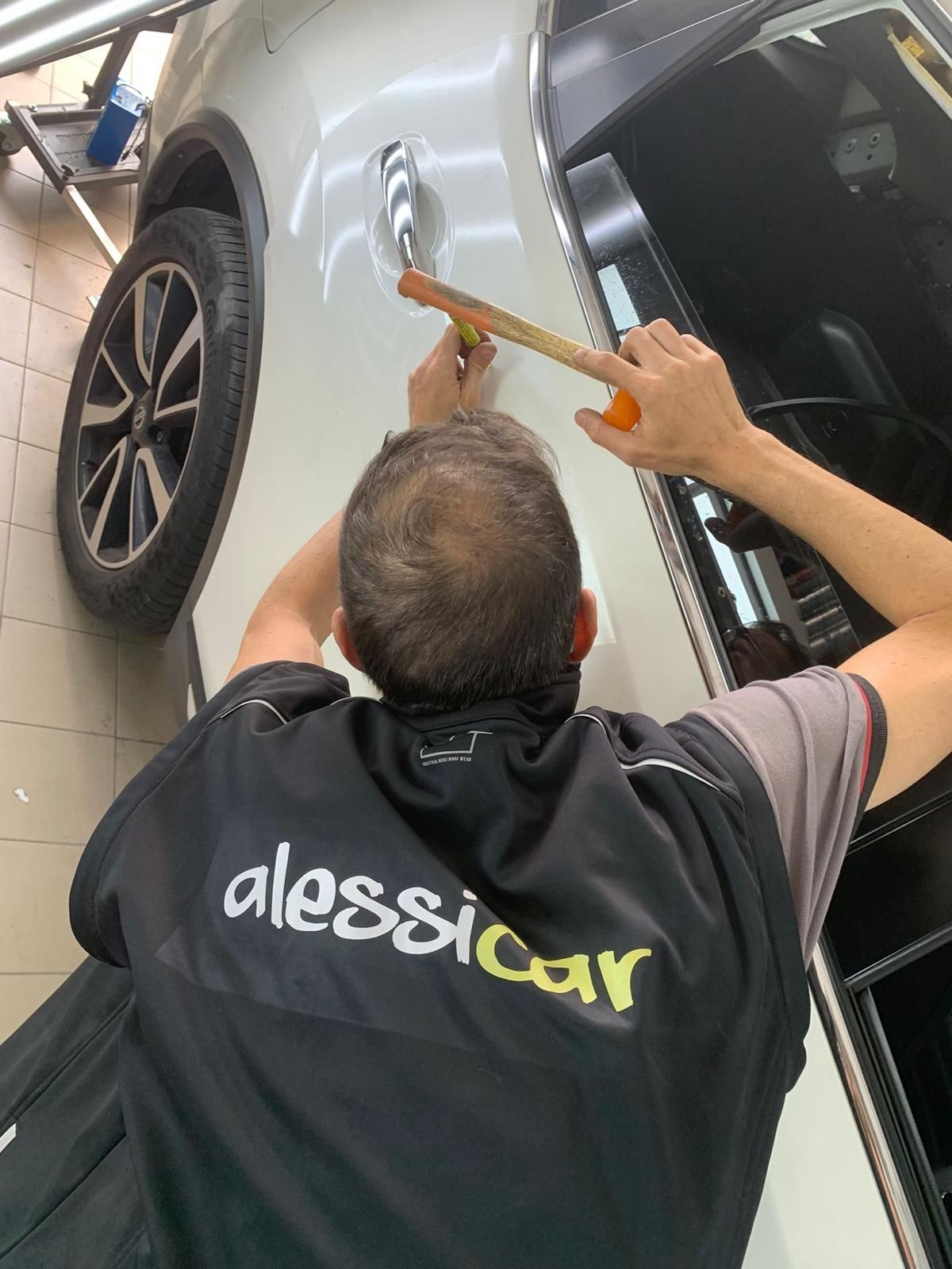 Persona che esamina il cofano di un'auto sotto una luce, probabilmente per riparare un'ammaccatura.