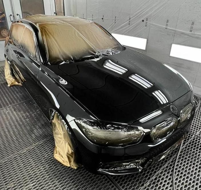 Auto nera in cabina di verniciatura, finestrini e finiture ricoperti, finitura lucida, pronta per i ritocchi finali.