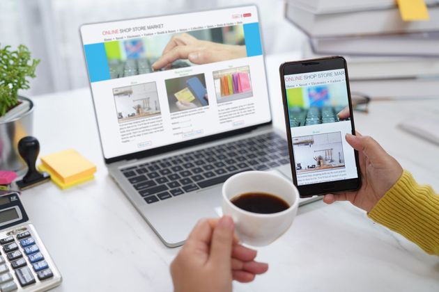 A person is holding a cup of coffee in front of a laptop and a cell phone.