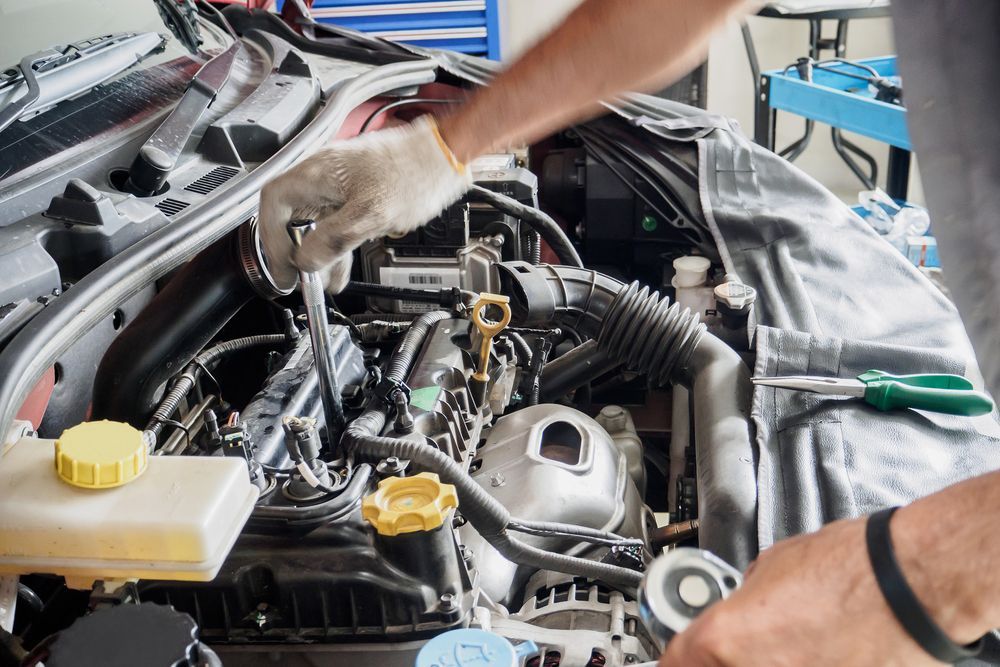Mechanic using a socket wrench to perform engine repairs on a car with the bonnet open in a workshop