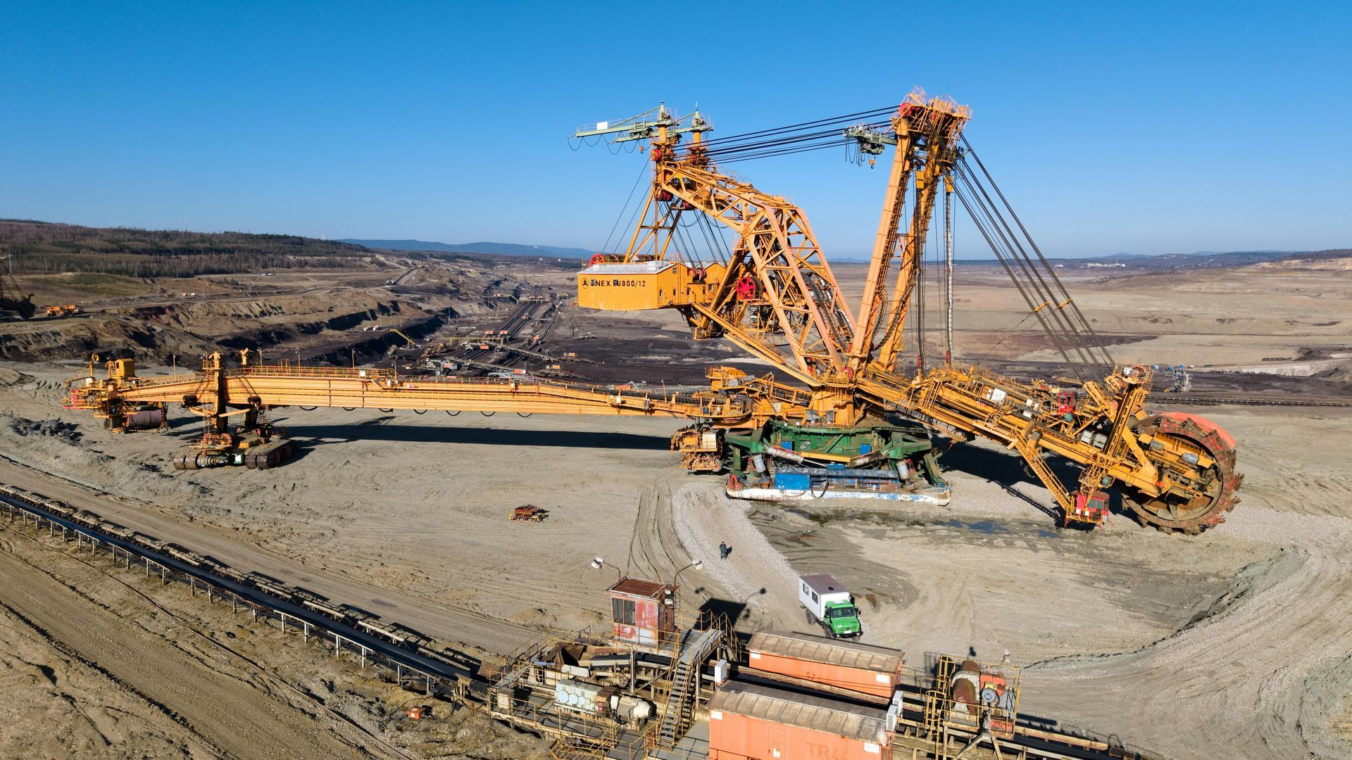 Large yellow bucket-wheel excavator in a barren landscape, working on a mine.