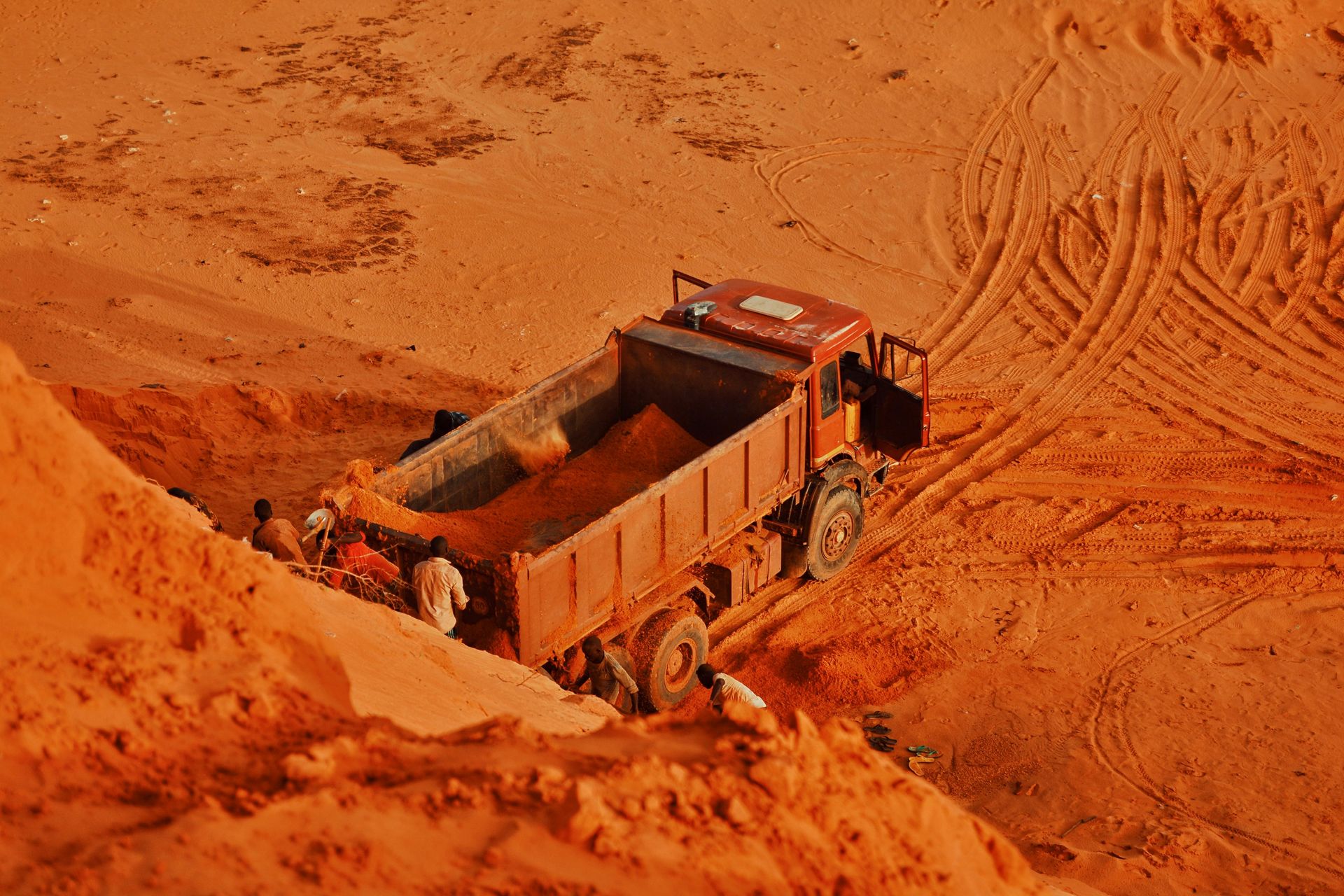 Red dump truck being loaded with material at a construction site in a desert setting.