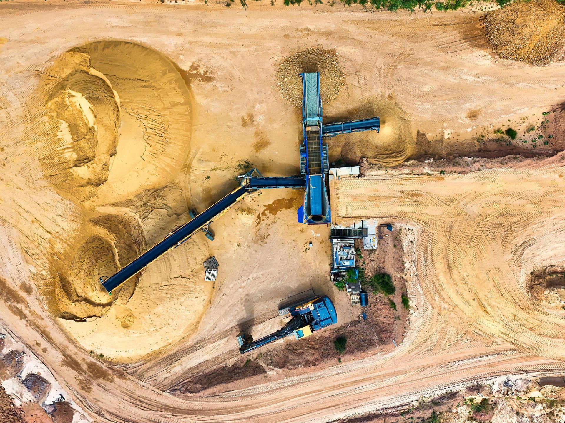 Aerial view of a sand processing site with machinery, conveyor belts, and large piles of sand.