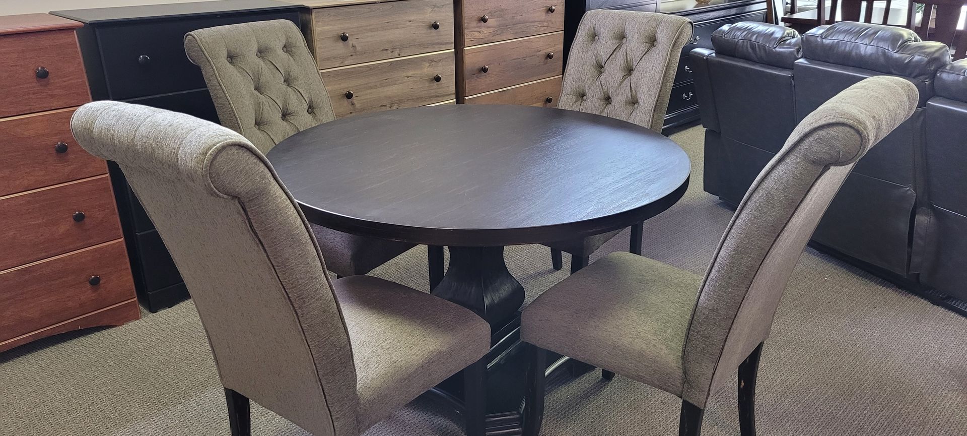 A round dining table with four upholstered chairs in a furniture showroom.