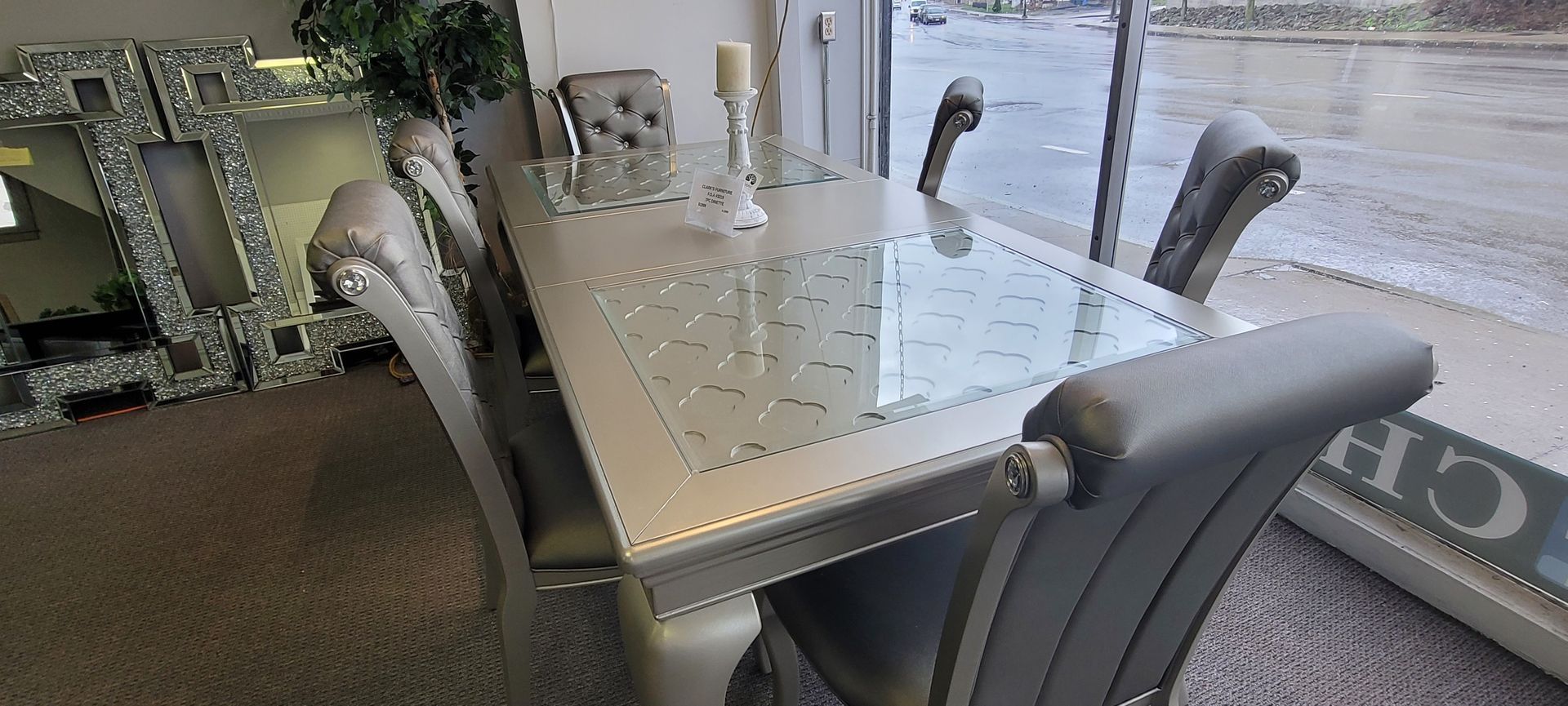 A dining table with grey chairs, a decorative mirror and view of a waterside area.