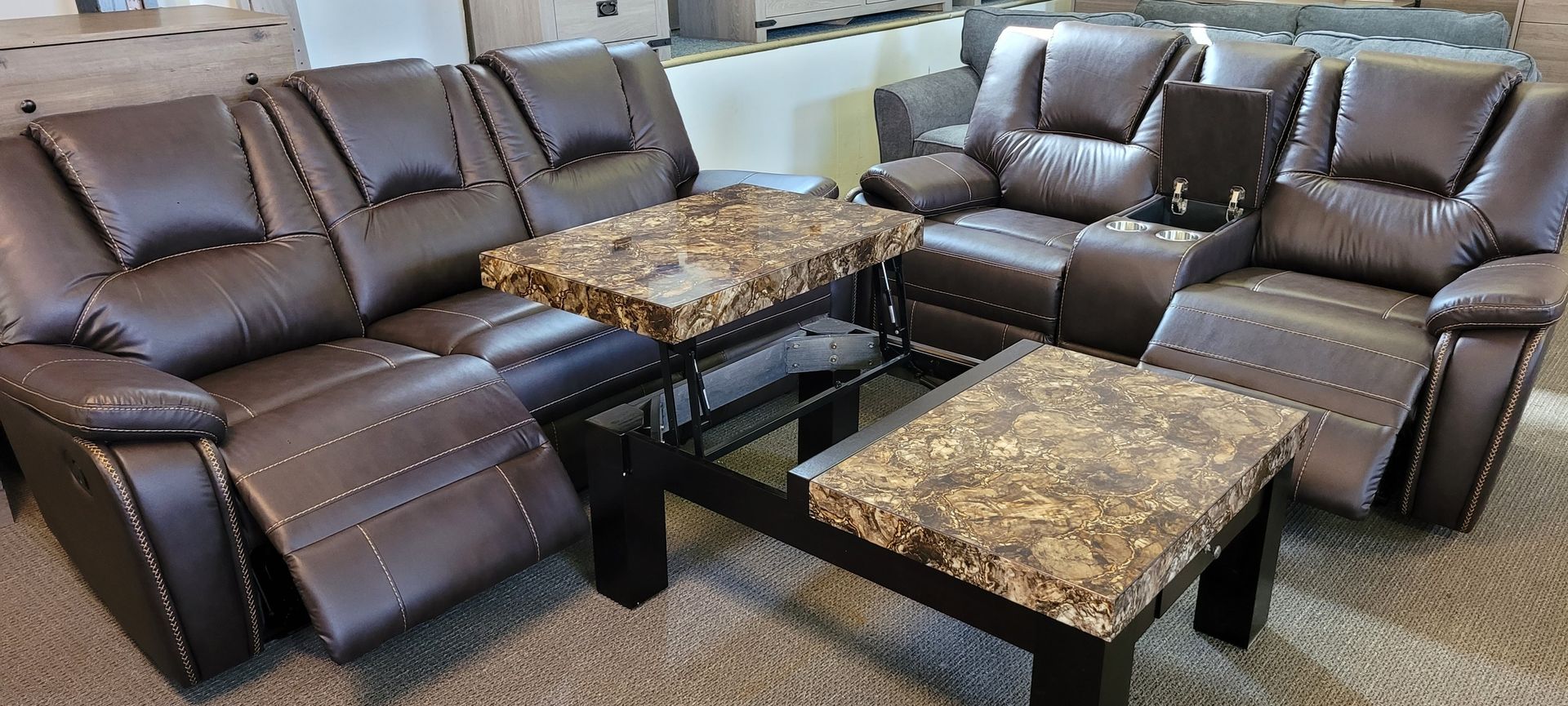 Brown leather reclining sofa set with a marble-top coffee table in a showroom setting.