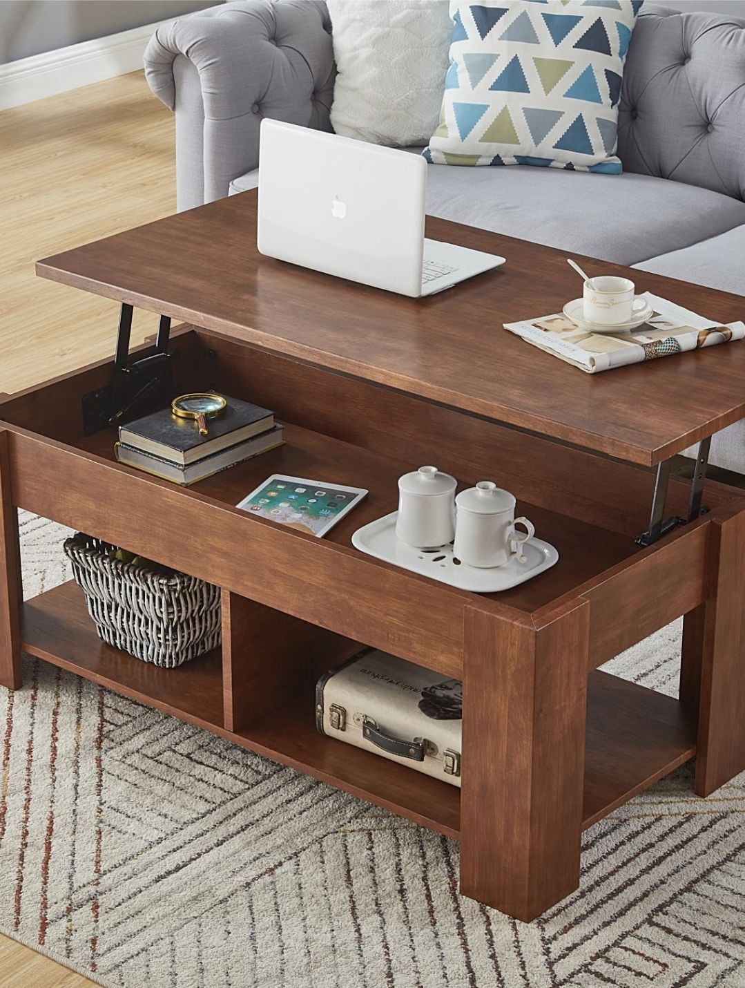 Wooden lift-top coffee table with a laptop, drinks, and decor, in a living room.