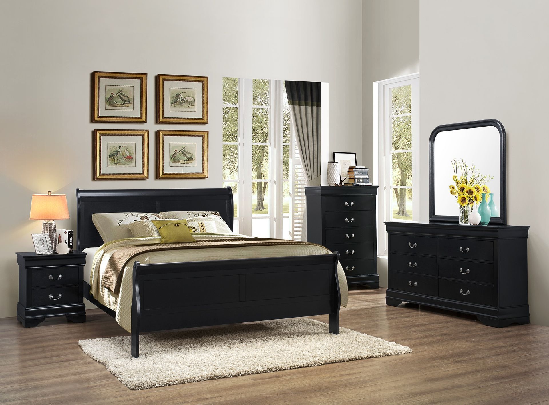 Black bedroom set with bed, nightstand, dresser, chest, and mirror in a bright room with art.