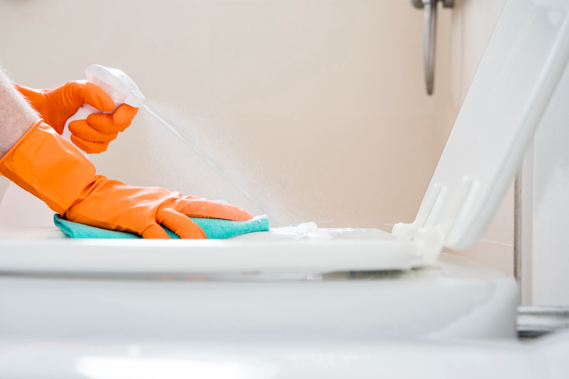 A person wearing orange gloves is cleaning a toilet
