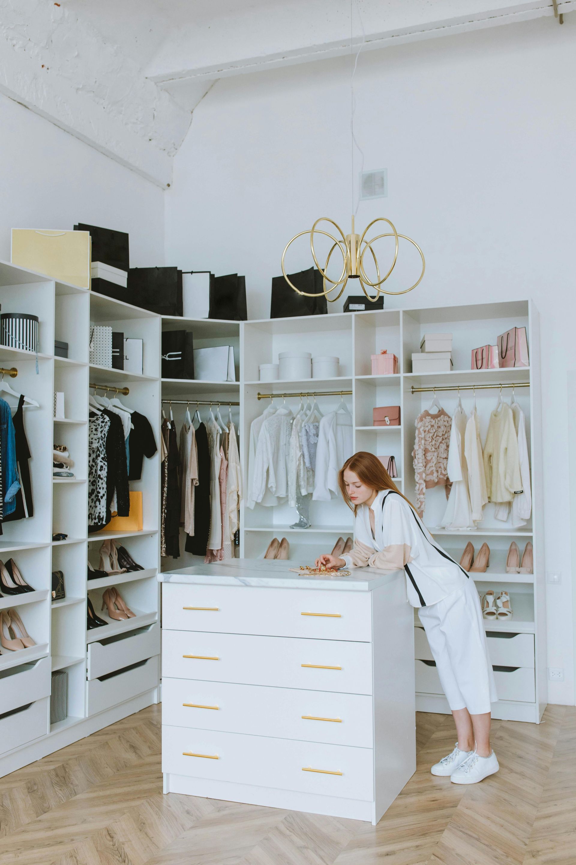 A woman is standing in a walk in closet looking at clothes.