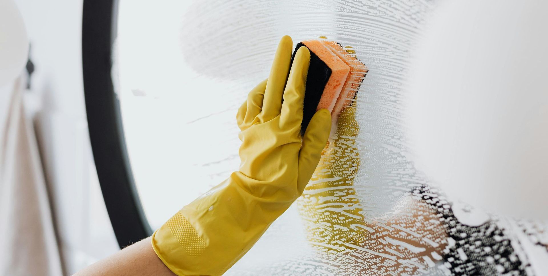 A person wearing yellow gloves is cleaning a window with a sponge.