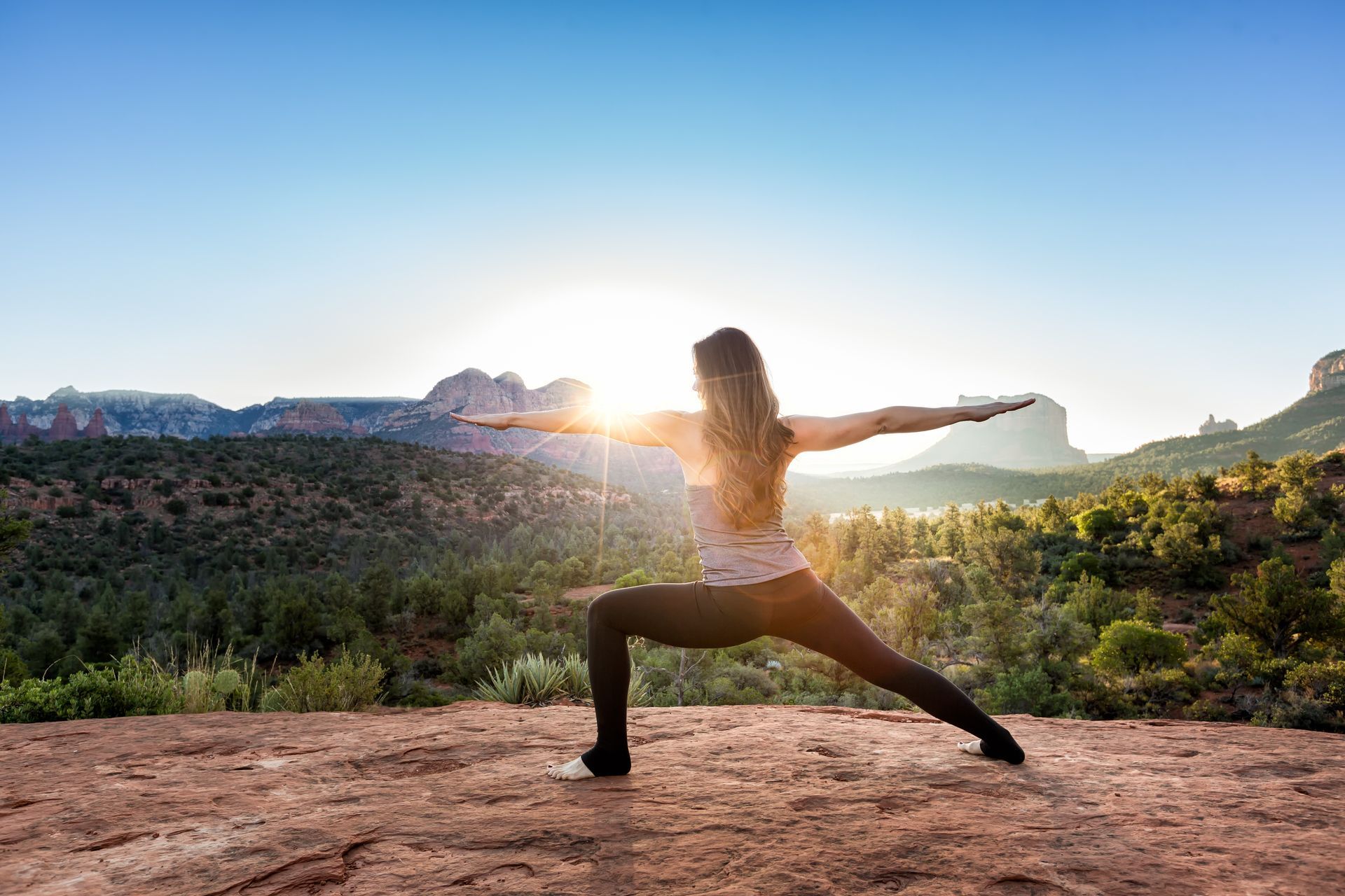 Person doing a yoga warrior pose outdoors at sunrise with mountains in the background