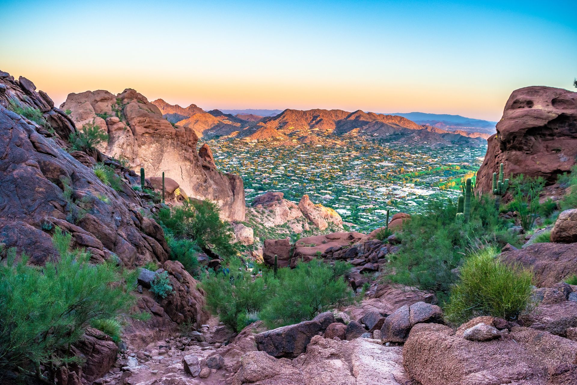 Rocky desert canyon at sunset overlooking a green valley and distant mountains