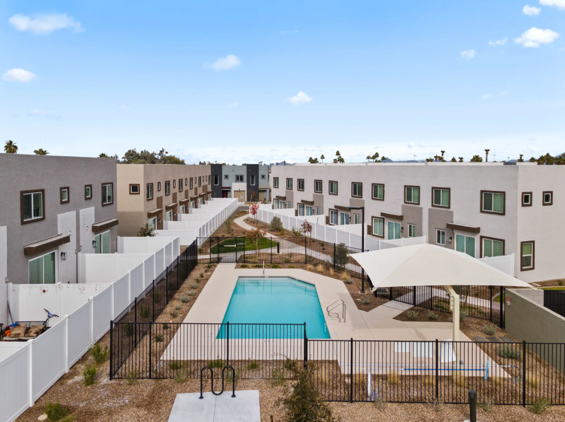 Modern apartment complex courtyard with a central pool and white umbrellas under a blue sky