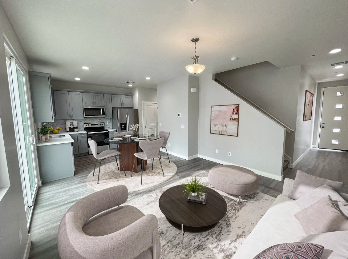 Bright open-concept living room and kitchen with gray walls, round coffee table, and staircase.