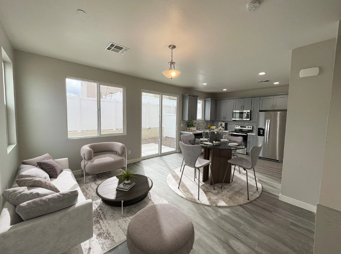 Bright open-concept living room with gray furniture, round coffee table, and kitchen in the background